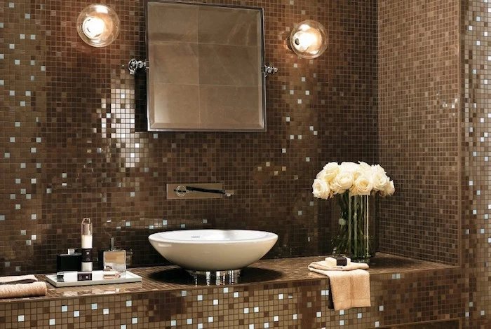 vase with white roses, two lamps and a mirror, and a round white sink, in a room with walls covered in mosaic, in different shades of brown, with tiny mirror details, bathroom wall decor ideas