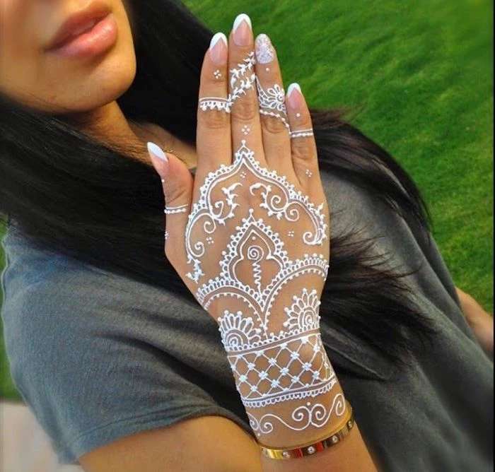 cuff made of gold, on the wrist of a brunette woman, dressed in a grey t-shirt, her hand is decorated with white mehndi