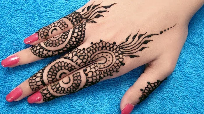 scale-like dark brown mehndi details, on a pale hand, with bubblegum pink nail polish, resting on a teal blue towel