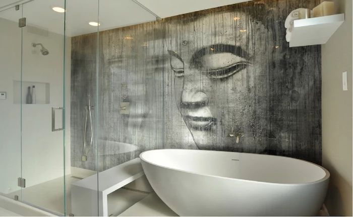 grey wall mural, depicting the face of Buddha, in a room with a glass shower cabin, and an oval white bathtub, bathroom wall decor ideas, of-white walls, and ceiling lights