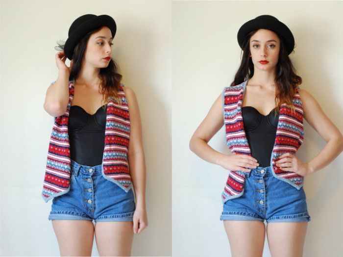 vest with a colorful pattern, worn over a black bustier, tucked into high waisted, button up denim shorts, on a young brunette girl, with a black hat