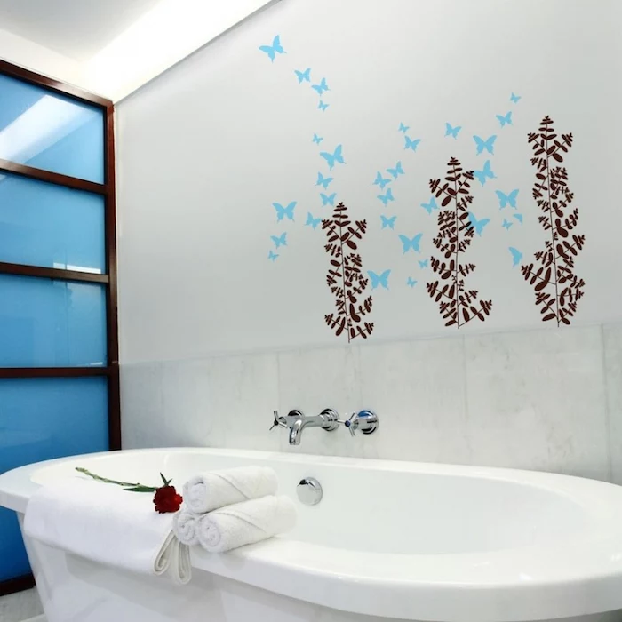 towels in white and a red rose, placed on a white oval bathtub, bathroom decorating ideas on a budget, nearby wall is decorated with blue and brown decal stickers, shaped like butterflies and plants