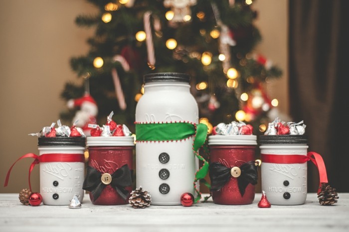 bows and buttons in black, and ribbons in red and green, decorating four small, and one large jars, painted in white and red, and filled with candy, creative gift ideas, christmas tree in the background