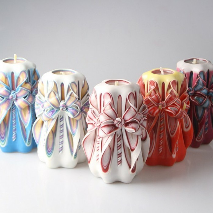 five large carved candles, in different colors, featuring bow-like details, on an off-white surface, cute birthday ideas