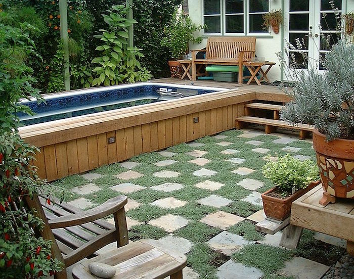wooden stool near a bench, in a garden with lots of flowers and shrubs, containing a rectangular pool, lined with beige planks