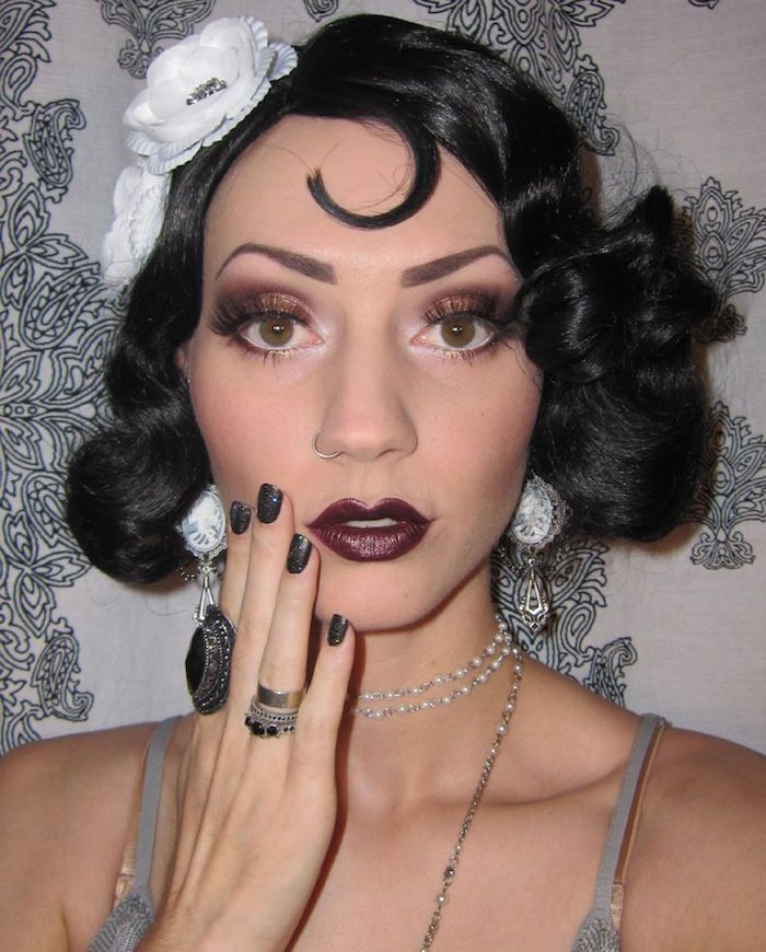 close up of a woman's face, with cherry red lipstick, purple eyeshadow and fake lashes, and black hair, styled in a 1920s bob