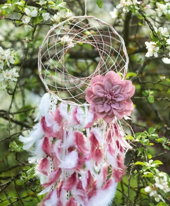 fluffy small feathers, in white and pink, attached to a dreamcatcher, decorated with a pink flower ornament, how to make a dreamcatcher, hung on a blossoming tree