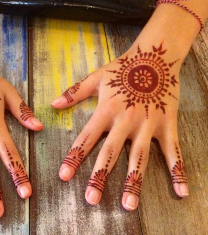 sun-shaped mandala, drawn on a child's hand, with brown henna, fingertip details with dots and lines