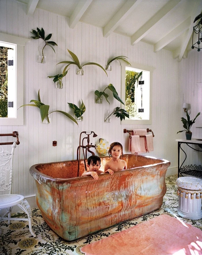 clear glass vases, mounted on a wall, covered in white wooden panelling, each containing different green leaves, diy bathroom décor, large vintage metal bathtub, with two small children