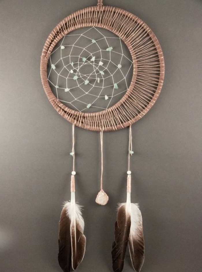 two chocolate brown and white feathers, and a small pink stone, tied to a rattan dreamcatcher, with a white net, decorated with pale blue beads, pictures of dream catchers, on a grey wall