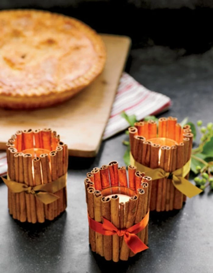 handmade gift ideas, sticks of cinnamon, placed around three candle holders, with lit candles, and tied with gold ribbons, a pie in the background