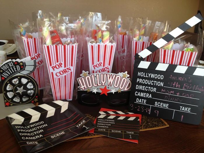 hollywood inspired decorations, like cardboard clapperboards and movie reels, 60th birthday ideas, several vintage-style popcorn boxes, white with red stripes, containing a selection of sweets