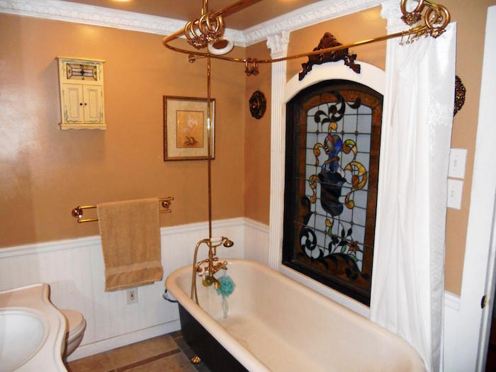 retro style bathroom, with beige walls, and white panelling, black and white oval bath, and a stained glass window, small bathroom décor, plaster details and a framed image 