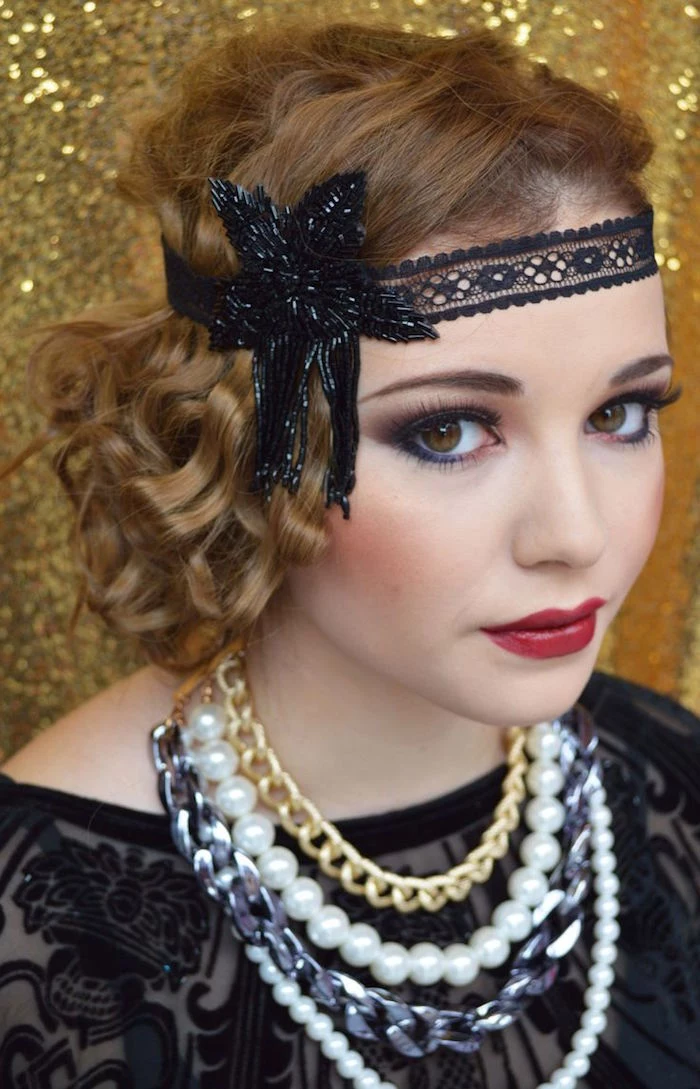 several chunky necklaces, and a black flapper headband, worn by a young woman, in sheer black lace top, and 1920s make up