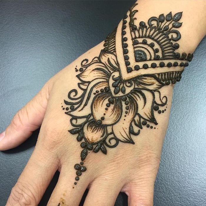 extreme close up of a person's wrist, freshly decorated with dark henna, featuring floral motifs and dots, henna hand tattoo designs