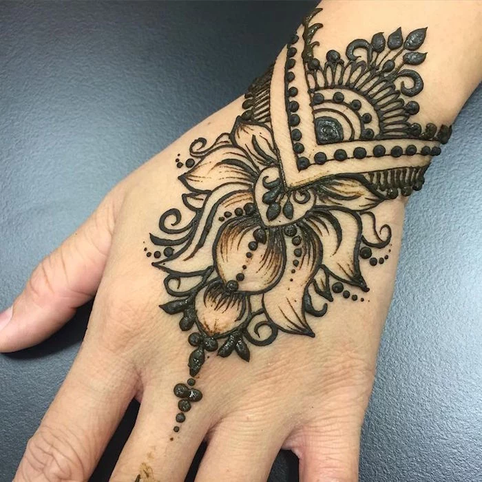 extreme close up of a person's wrist, freshly decorated with dark henna, featuring floral motifs and dots, henna hand tattoo designs