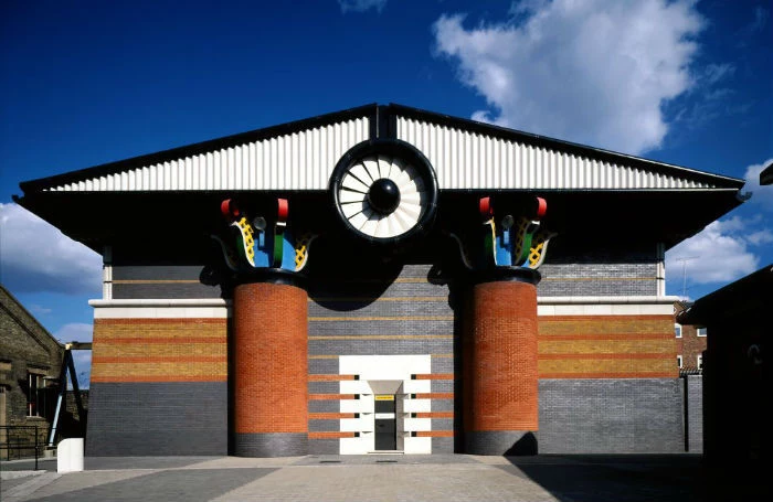 flattened gabled roof in black and white, propped on yellow and grey round columns, decorated with multicolored details on top, postmodernism examples, orange and grey pumping station building