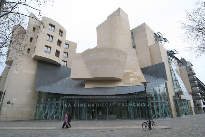 abstractly shaped building, covered in cream and pale beige tiles, with a grey roof-like detail, and a glass entrance, postmodern buildings, la cinematheque francais in paris