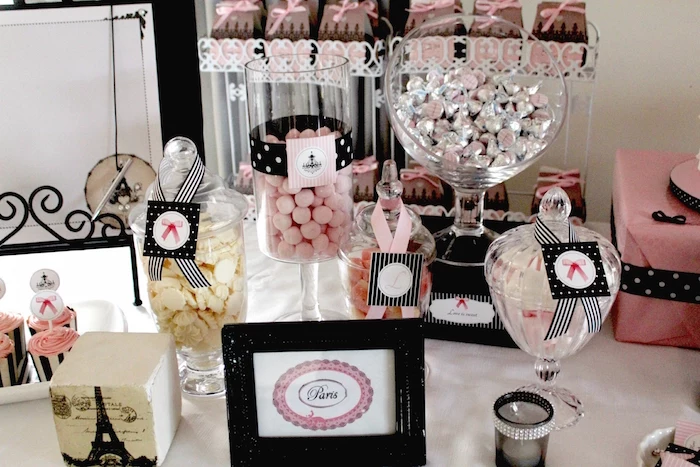 jars and other glass dishes, containing candies in pink, cream and silver, on a parisian-themed party table, 60th birthday party ideas for mom, little eiffel tower decoration