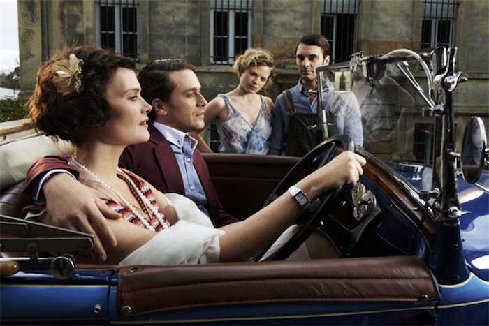 convertible blue antique car, with brown leather interior, driven by a young woman with bobbed hair, hugged by a man in a mauve blazer, roaring 20s fashion, another couple in the background