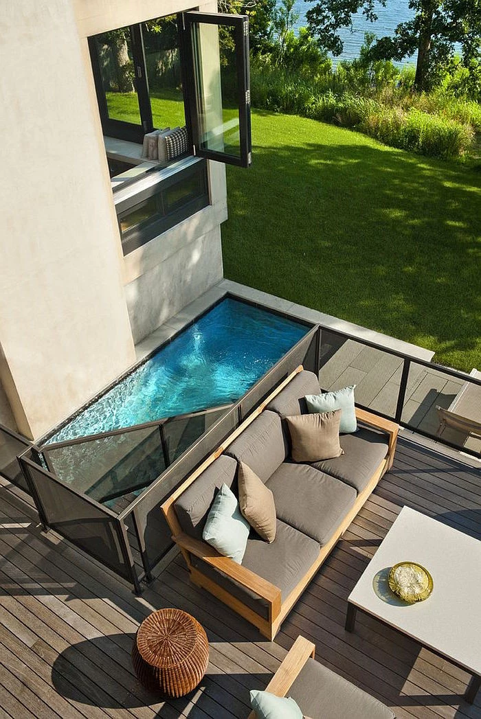 modern small pool, with a metal divide, surrounded by wooden planks, in a garden, containing a sofa and a table, cool backyards, house with an open window nearby