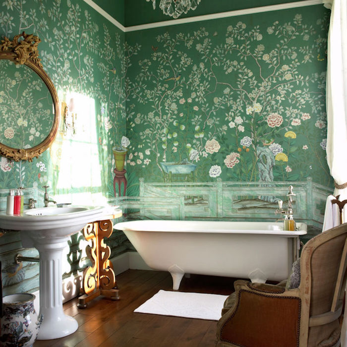 roses and trees, painted on the green walls of a bathroom, decorated in antique style, wooden floor and ornate sink, antique chair and a tub 