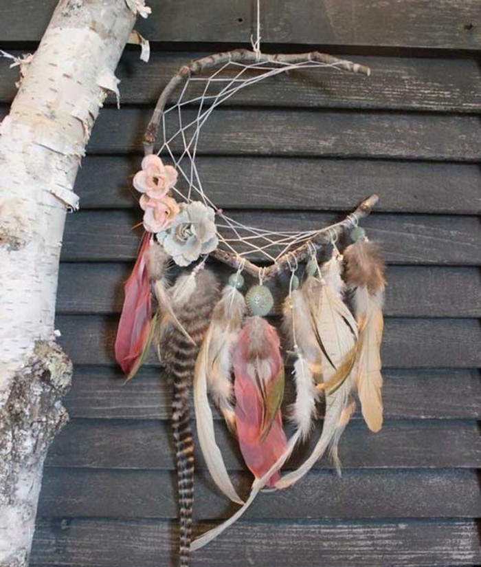 coral pink and beige feathers, some with patterns, tied to a crescent moon-shaped diy dreamcatcher, with several flower ornaments, in pale pink and blue