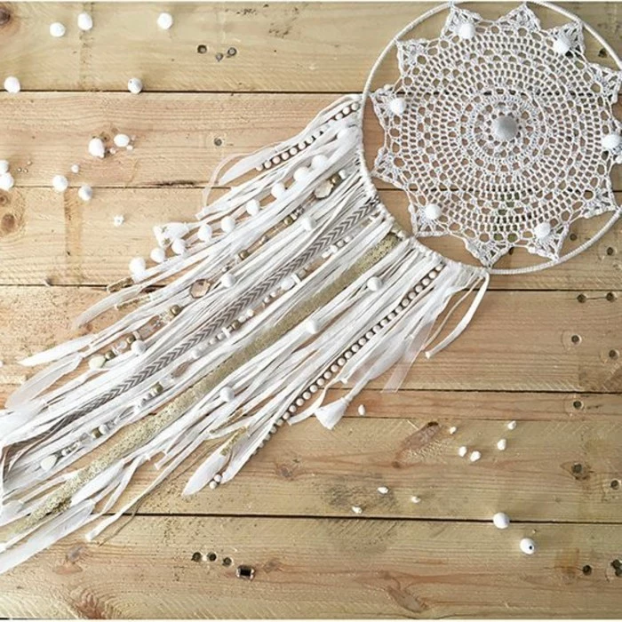 beads in white, a crochet off-white doily, and many ribbons in cream and white, boho dreamcatcher designs, pale wooden floor 