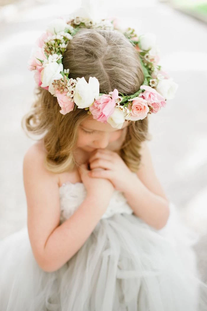 wreath made of white, and pale pink flowers, on the head of a child, with medium long, dark blonde hair, hairstyles for little girls, wearing an off-white tulle dress