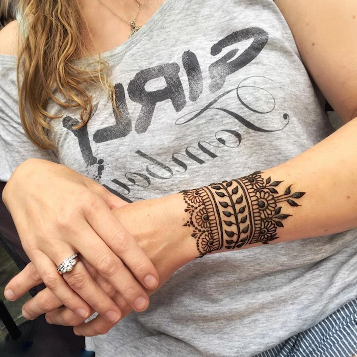 bracelet painted on a woman's wrist, using dark henna, leaves and flowers, henna meaning, pale grey top, and a silver diamond ring