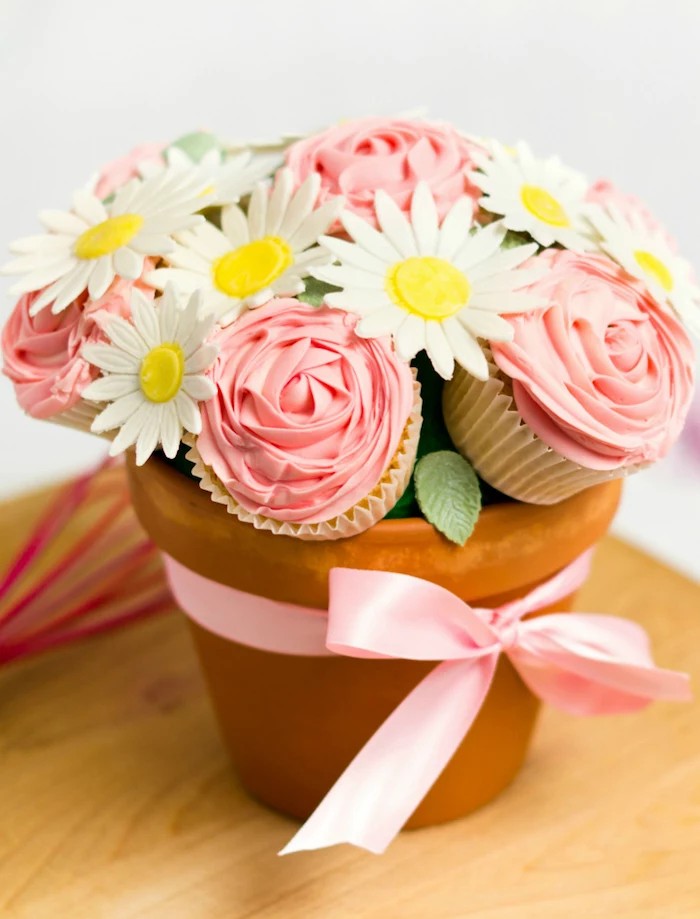 cupcakes and faux sunflowers in ceramic pot, creative diy christmas gifts, pink satin ribbon around, placed on wooden table