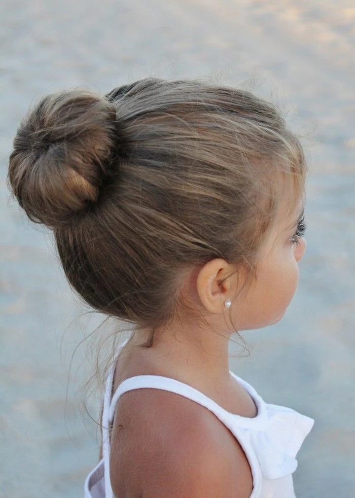 ballerina hair bun, on the head of a small brunette child, cute hairstyles, wearing a white frilly top