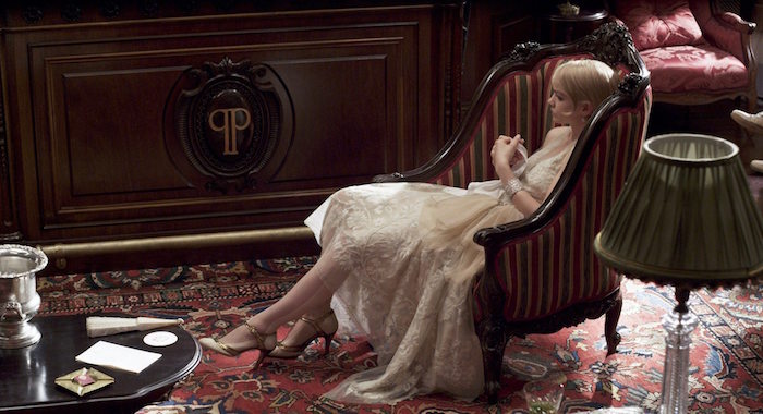 carey mulligan as daisy buchanan, wearing a light cream, embroidered silk dress, with a cream tulle side bow, and t-bar shoes, sitting in an antique armchair, great gatsby outfits
