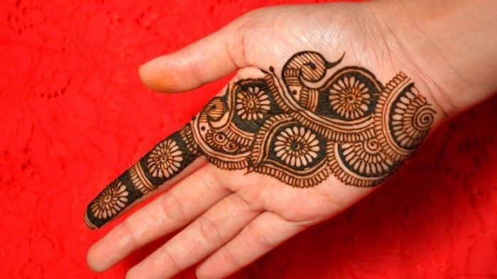 floral patterns on the palm of a hand, dark brown finger henna, with daisy-like shapes, running down to the wrist 