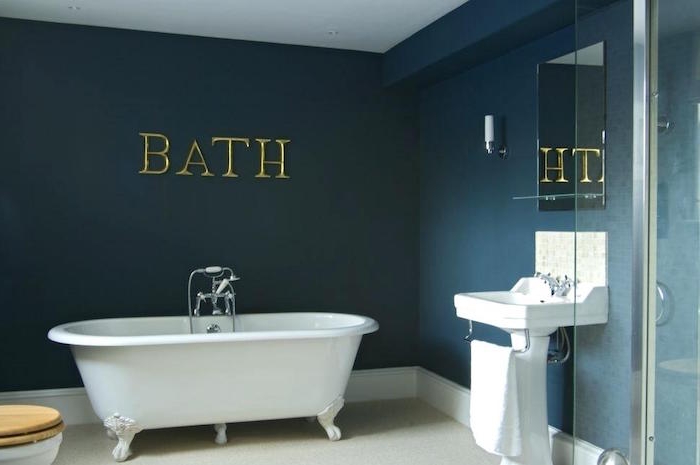 the word bath, spelled in large gold letters, on a dark ocean blue wall, diy bathroom decor, white claw-footed bathtub, and matching white sink