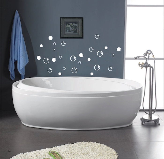 stickers in white, shaped like bubbles, on a dark grey wall, near a modern, white oval bathtub, bathroom decorating ideas on a budget, fluffy cream rug, pale blue towel