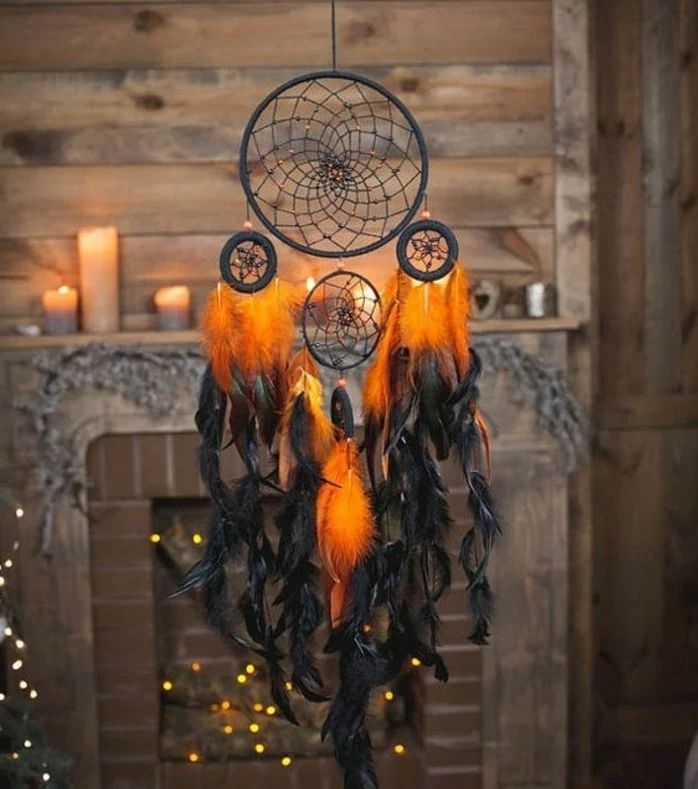 orange and black feathers, hanging from a black dream catcher, with four nets, how to make a dreamcatcher, fireplace with lit candles on the mantelpiece 