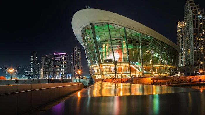 boat-shaped structure, made of glass and metal beams, with an oval white roof, dubai opera house, lit from within, post modernity 