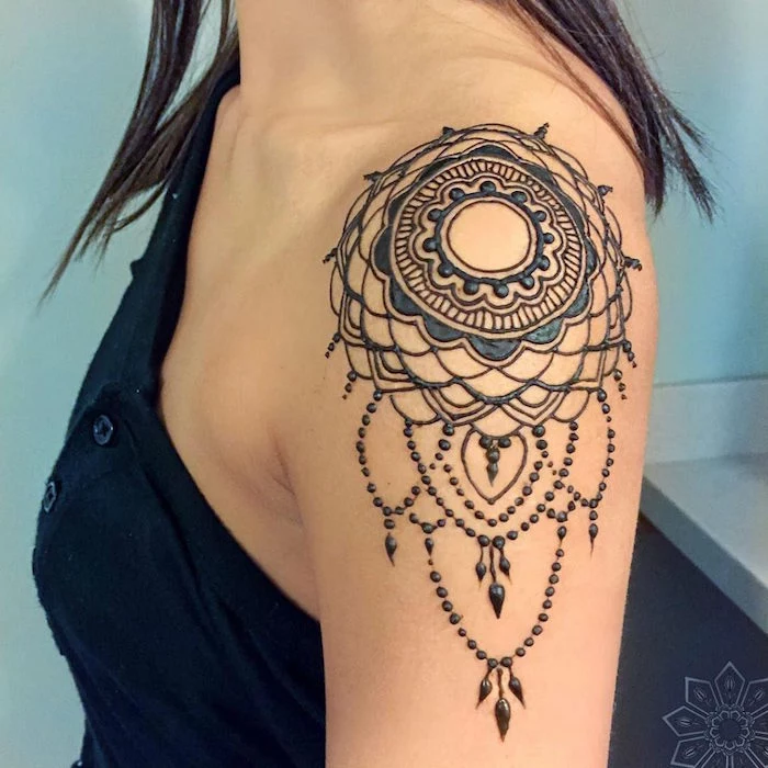 shoulder tattoo with a circular pattern, painted with dark henna, cute henna designs, worn by a brunette woman, in a black top