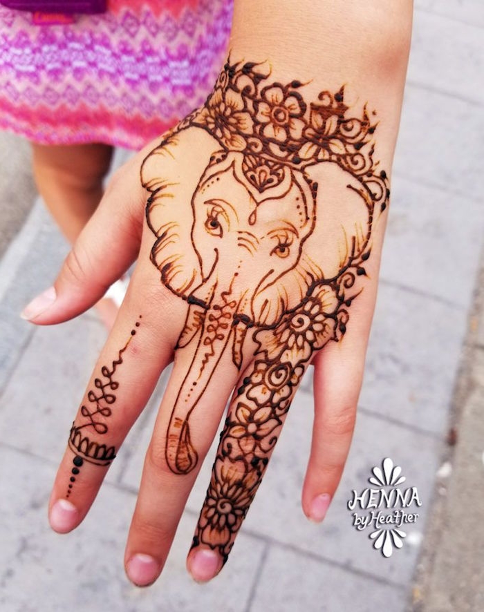 child's hand decorated with a drawing of an elephant, surrounded by flowers, all done in brown henna