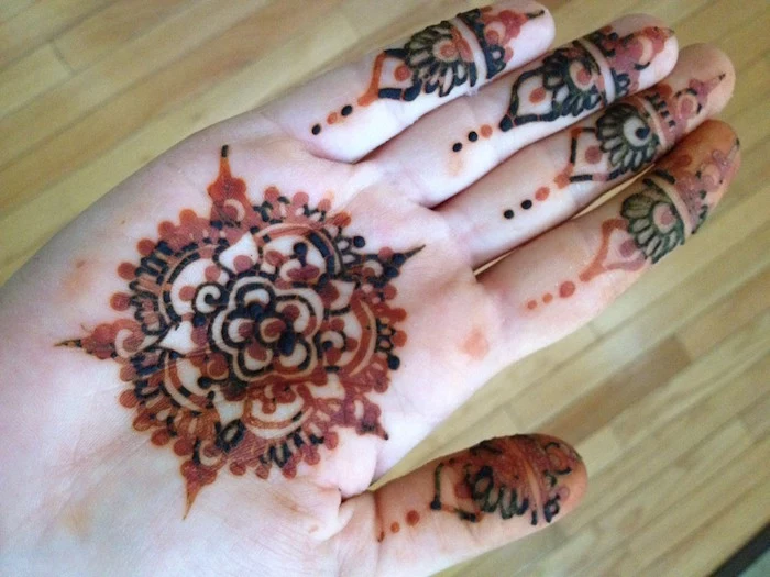 mehndi in dark brown and orange, fading from the palm of an outstretched hand, mandala motif and finger details