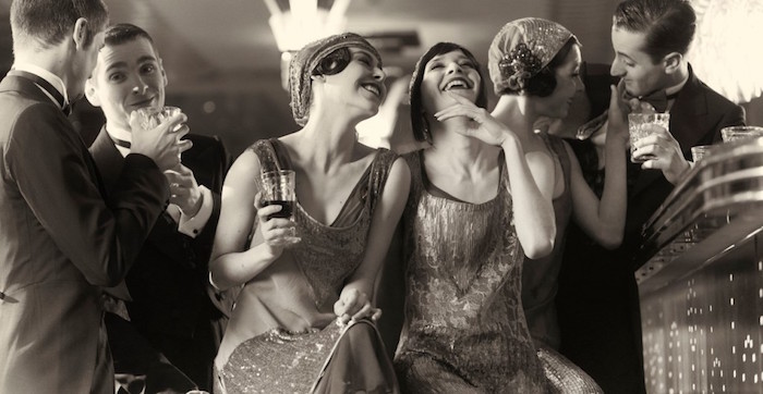 mock-antique black and white photo, featuring laughing and talking young people, dressed in roaring 20s dress, and holding glasses