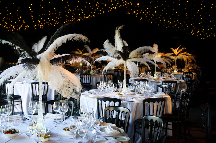 ostrich feather centerpieces, on several tables, set for a fancy dinner, with white tablecloths, and black chairs, 60th birthday party ideas, roaring 20s inspired setup