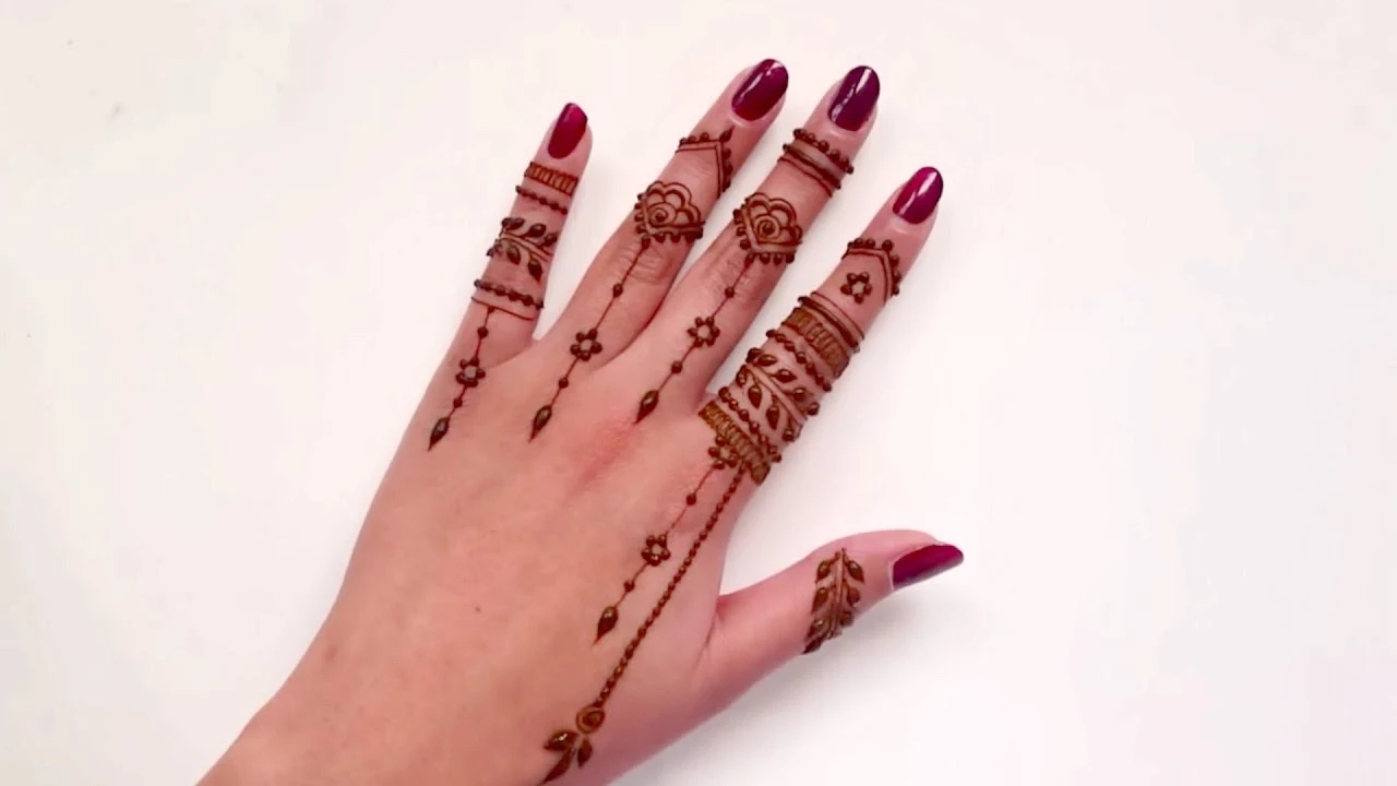surface in white, with a hand, wearing dark red nail polish, and freshly made, dark brown finger henna 
