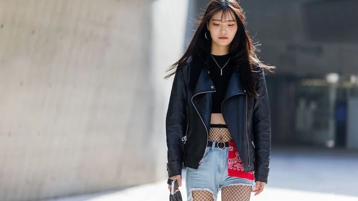 biker leather jacket in black, worn over a black cropped top, 90s clothes womens, girl in denim shorts, and fishnet tights