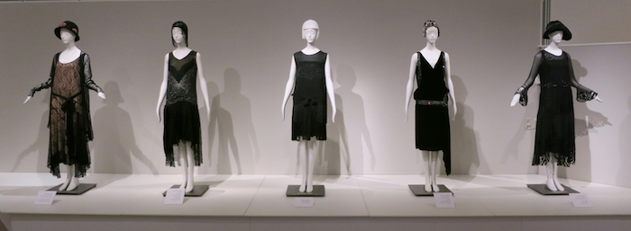 examples of roaring 20s dress, five gowns in brown and black, featuring low waists, fringe details and embroidery, worn by mannequins