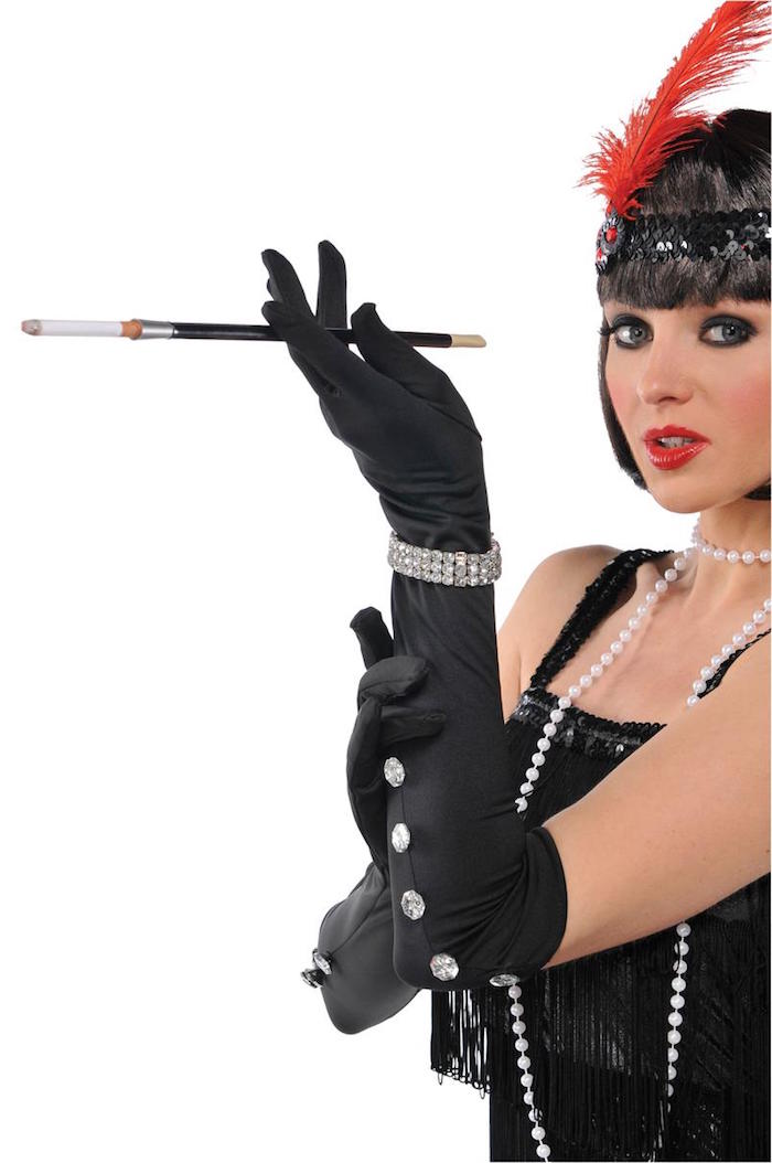 black fringed dress, worn with long black satin gloves, decorated with diamante jewelry, on a woman with a black headband, featuring a red feather, great gatsby costumes, long pearl necklace