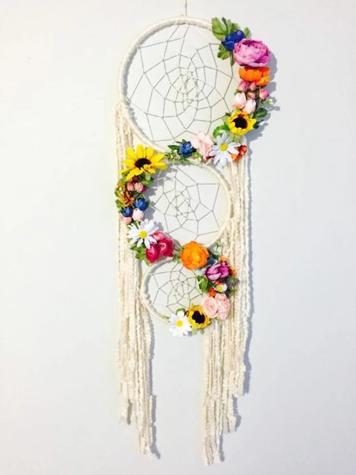 variety of flowers in different colors, decorating a white dream catcher, with tree nets, and long off-white tassels