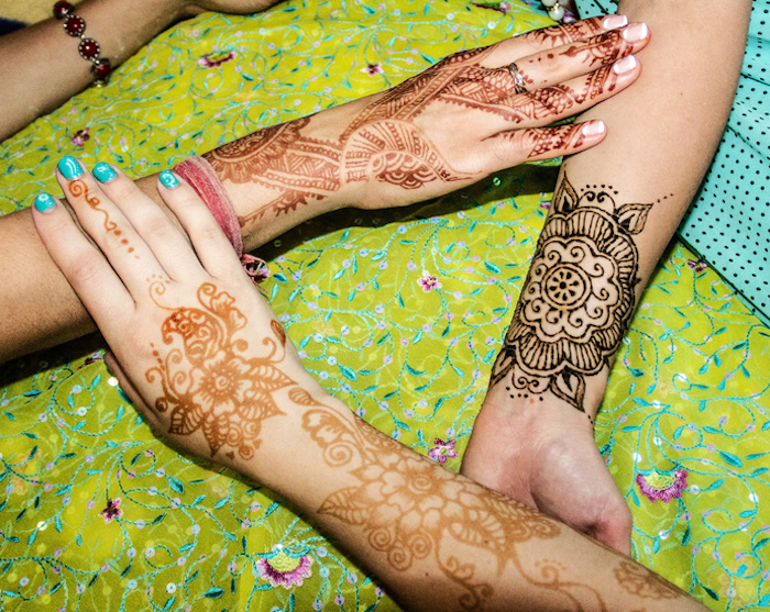 stages of mehndi, on three linked arms, just applied dark brown henna patterns, newly done pale orange mehndi, and a day old, light brown henna tattoo