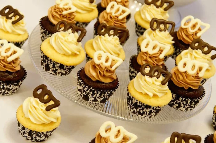 vanilla and chocolate cupcakes, in black and white wrappers, with cream and beige frosting, and white and dark chocolate toppers, shaped like the number 007 